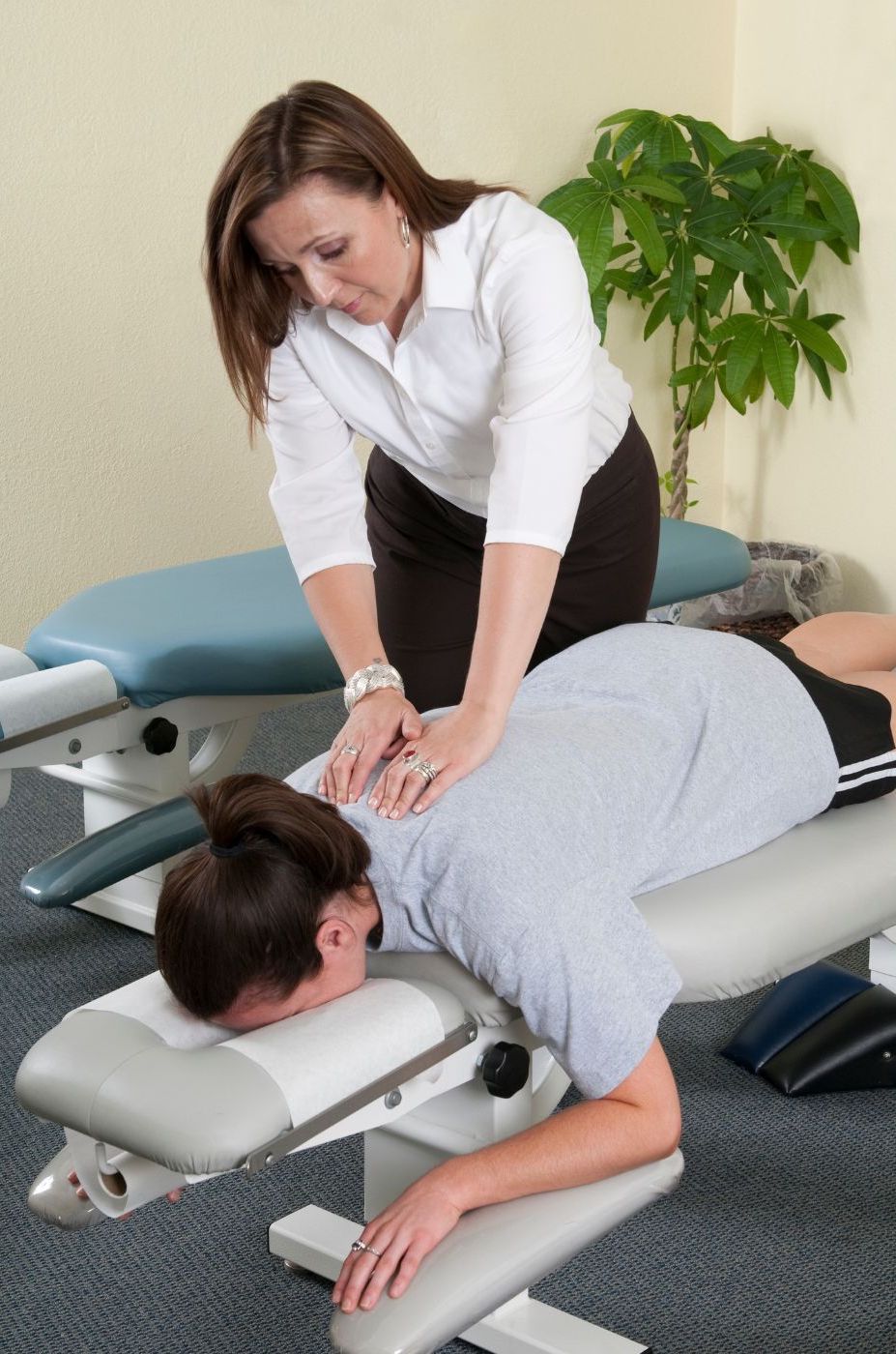 A chiropractor specializing in chiropractic care in Manhattan, a Caucasian woman in a white blouse, performs a spinal adjustment on a patient lying face down on a treatment table in a clinic. A chiropractor specializing in chiropractic care in Manhattan, a Caucasian woman in a white blouse, performs a spinal adjustment on a patient lying face down on a treatment table in a clinic.
